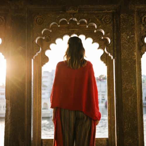 Estudiante observando un paisaje desde una ventana de arquitectura tradicional india durante un viaje educativo.