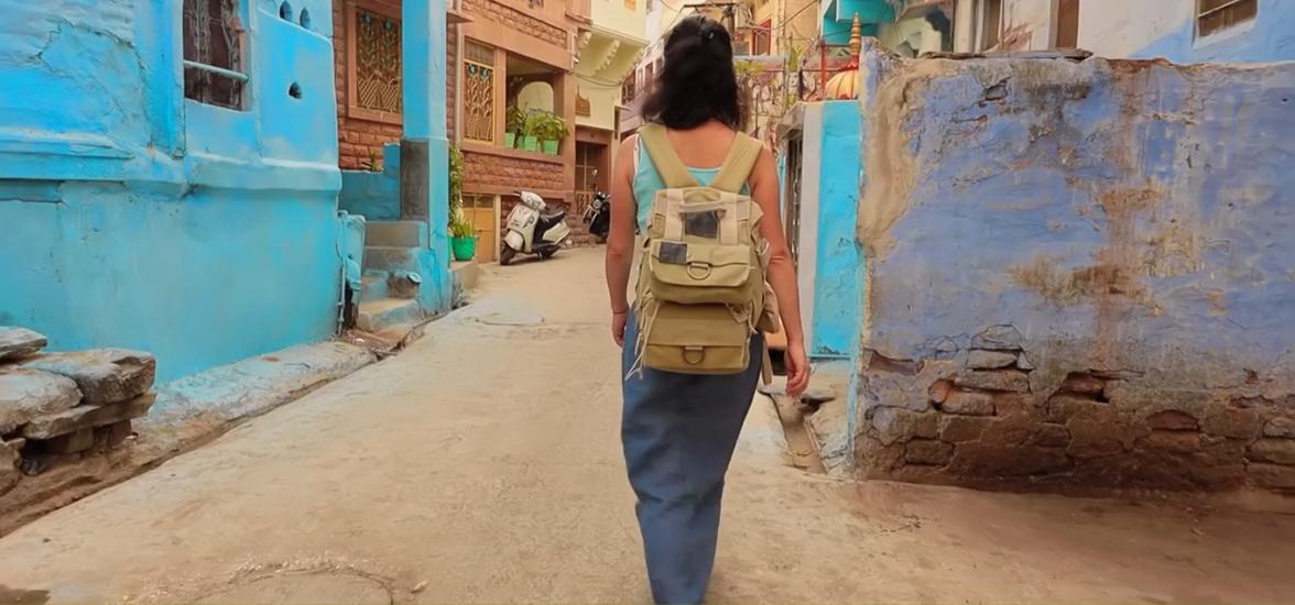 Female traveler walking through a traditional street in India, surrounded by colorful houses and a local atmosphere.
